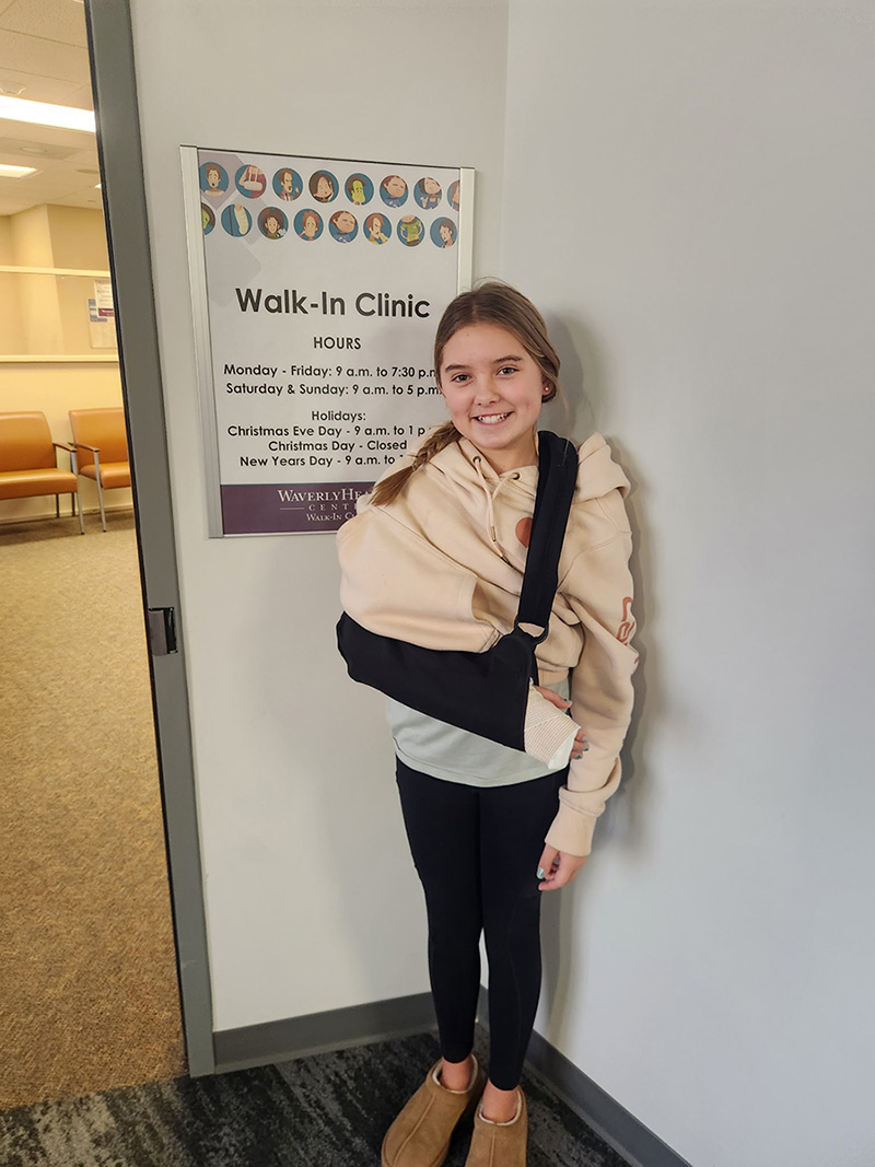 Big sister with sling smiling in front of Waverly Walk in Clinic